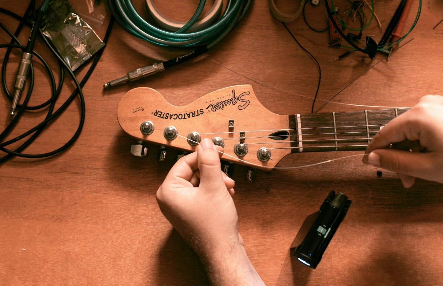 Hände besaiten eine E-Gitarre auf einer Werkbank neu.